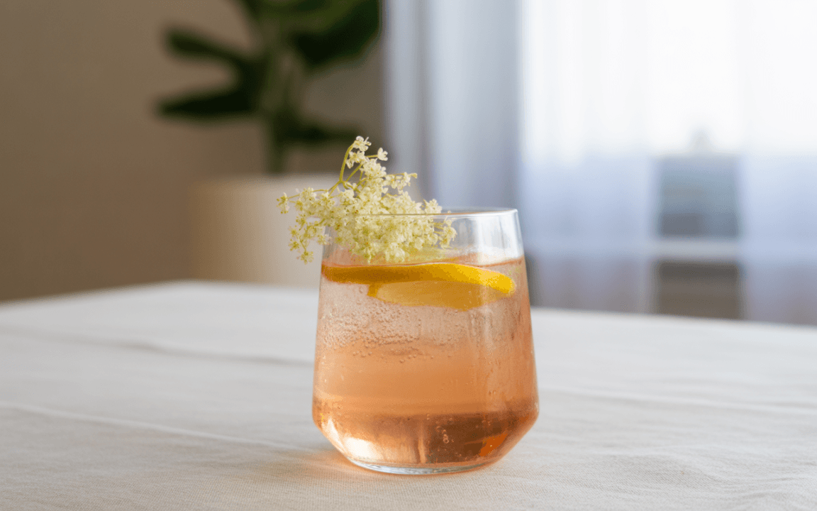 Verre de boisson pétillante rose avec des tranches de citron et une fleur blanche, sur une table claire et lumineuse.