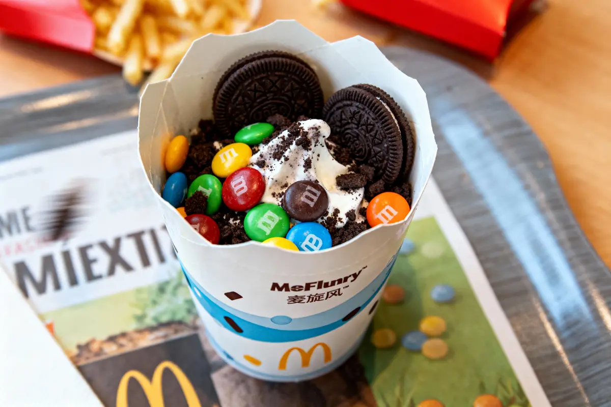 McFlurry avec Oreo, M&M's colorés et crème glacée, sur plateau avec frites en arrière-plan chez McDonald's.