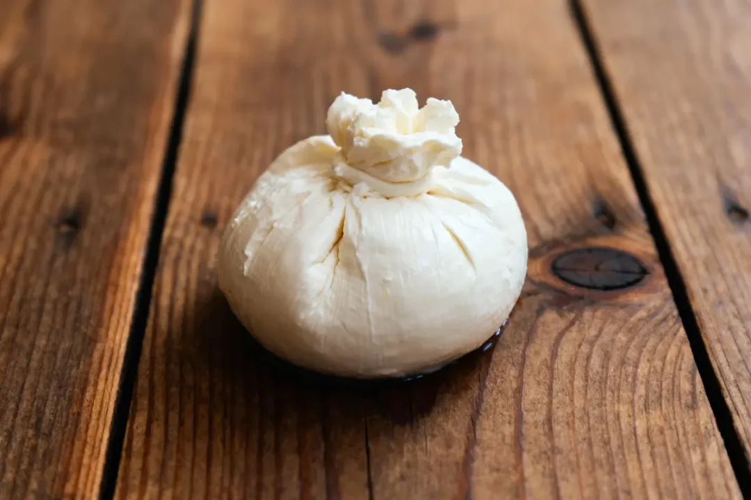 Fromage frais en boule sur une table en bois rustique, avec une texture crémeuse et plissée.