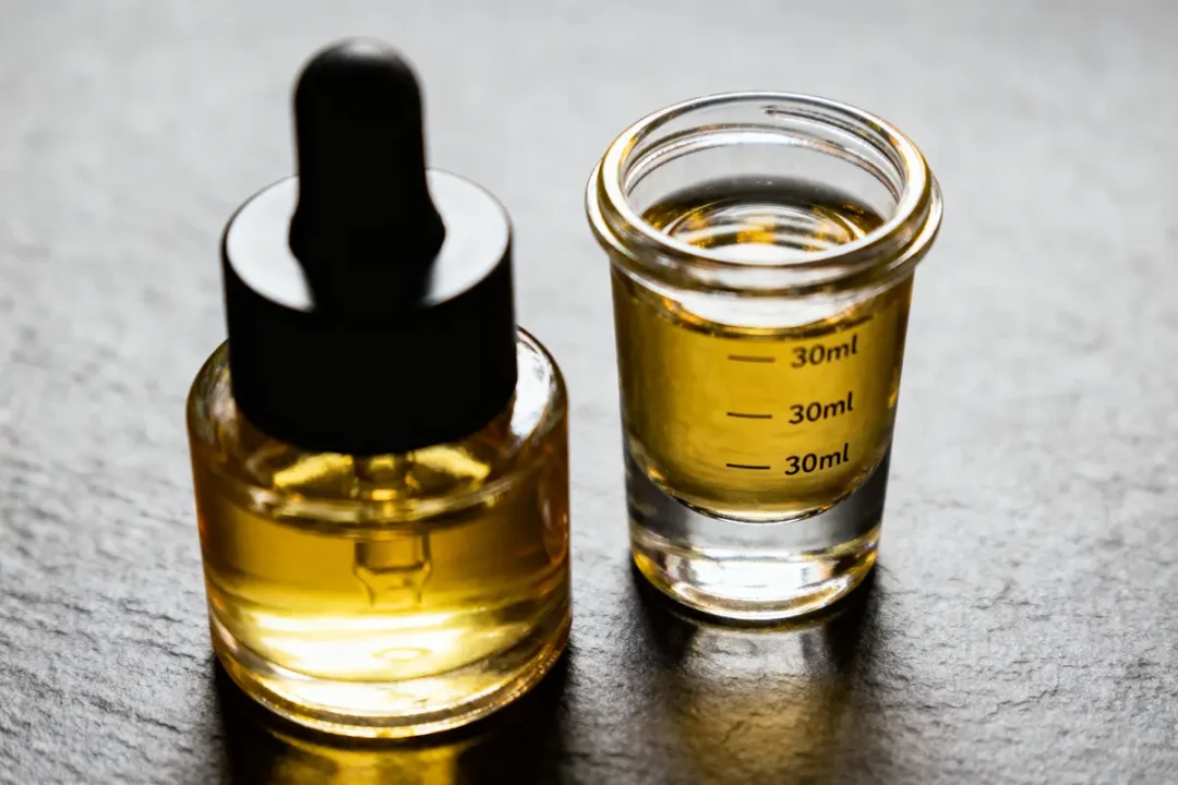Bouteille avec compte-gouttes et verre gradué contenant un liquide doré, sur fond sombre.
