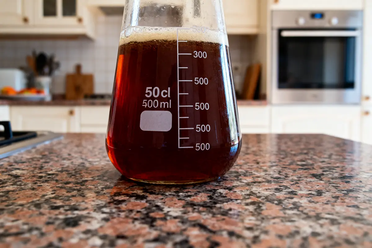 Flacon gradué contenant liquide brun, posé sur un plan de travail en cuisine moderne avec four.