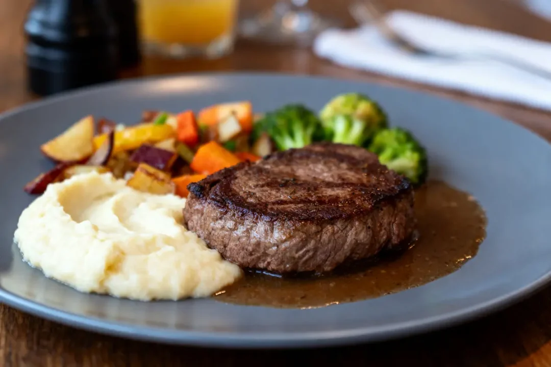 Assiette de steak grillé, purée de pommes de terre, légumes sautés et brocoli, sur table en bois.