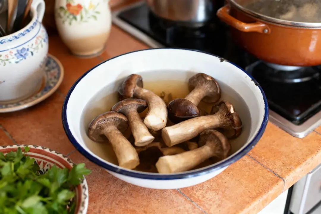 Bol de champignons trempant dans l'eau sur une cuisine rustique, herbes fraîches à gauche.