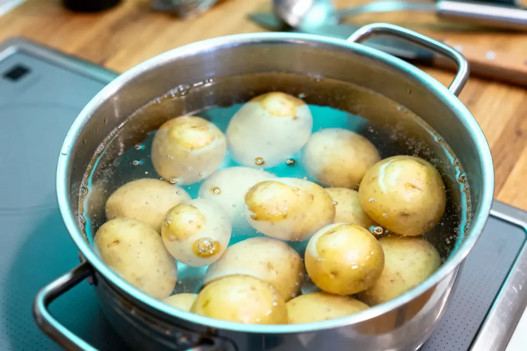 Casserole avec pommes de terre bouillant dans l'eau sur cuisinière, ustensiles en arrière-plan.