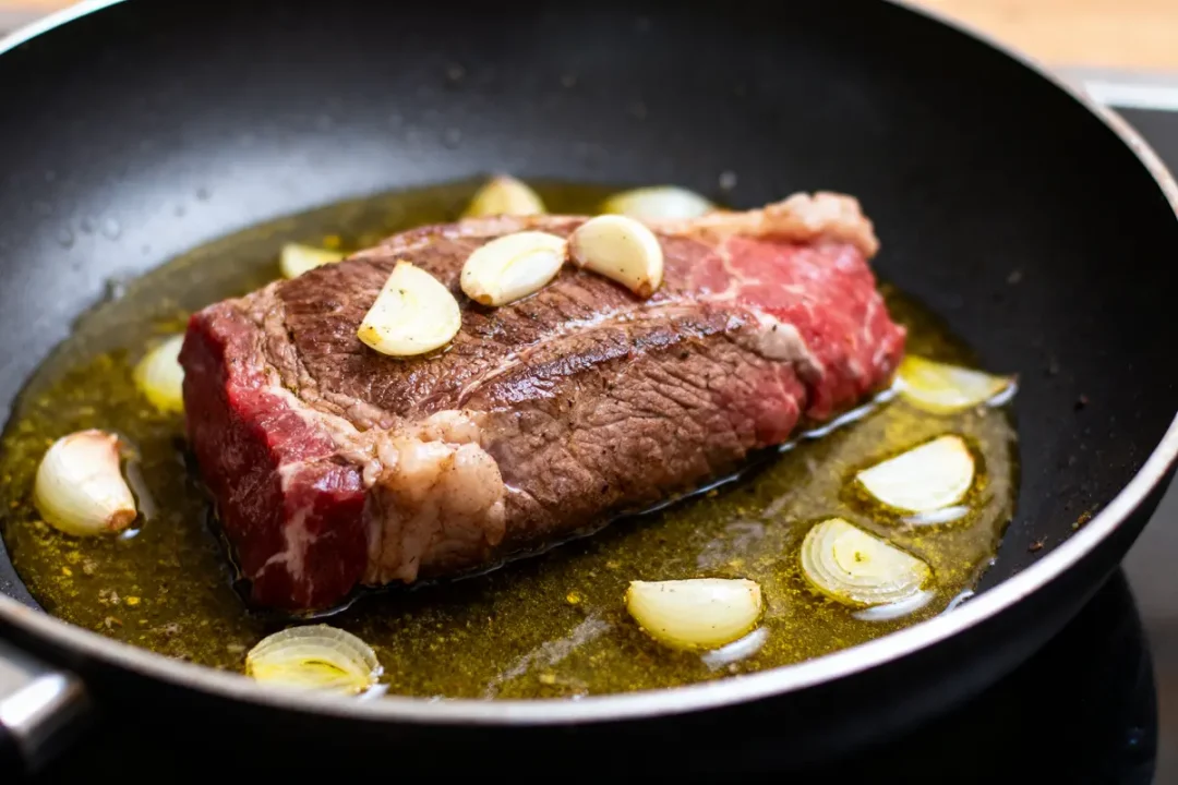 Steak saisi à la poêle avec ail et oignons dans l'huile.