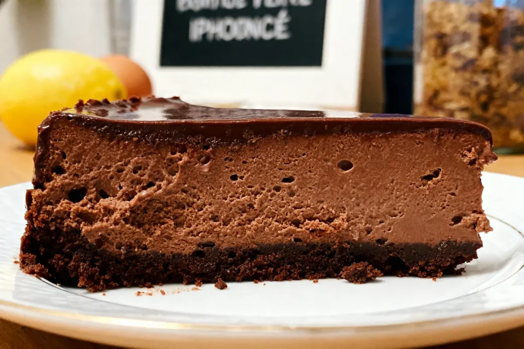 Tranche de gâteau au chocolat épaisse avec croûte, sur une assiette, fond flou.