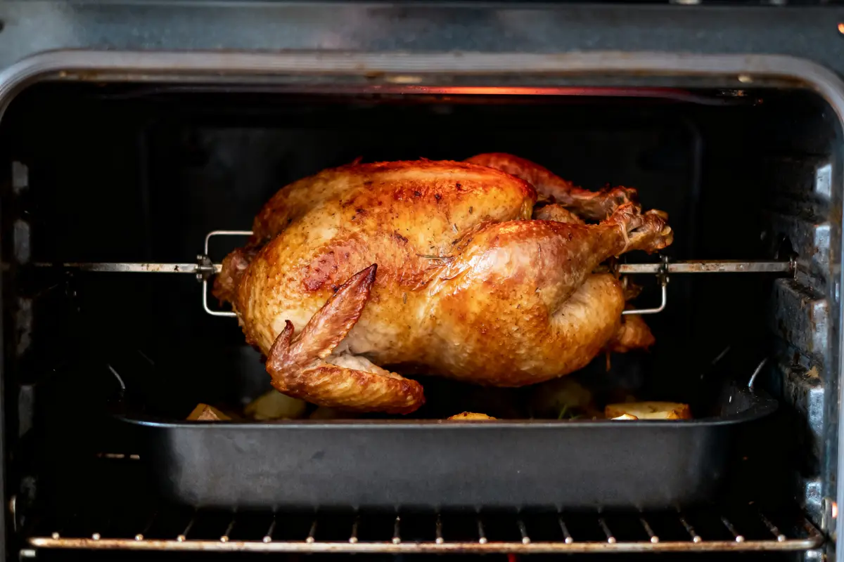Poulet rôti sur une rôtissoire dans un four, avec des pommes de terre en dessous.