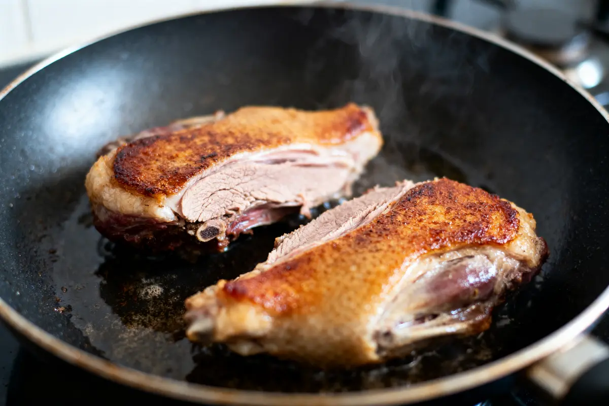 Deux magrets de canard poêlés, cuits à la perfection dans une poêle noire, avec une croûte dorée.