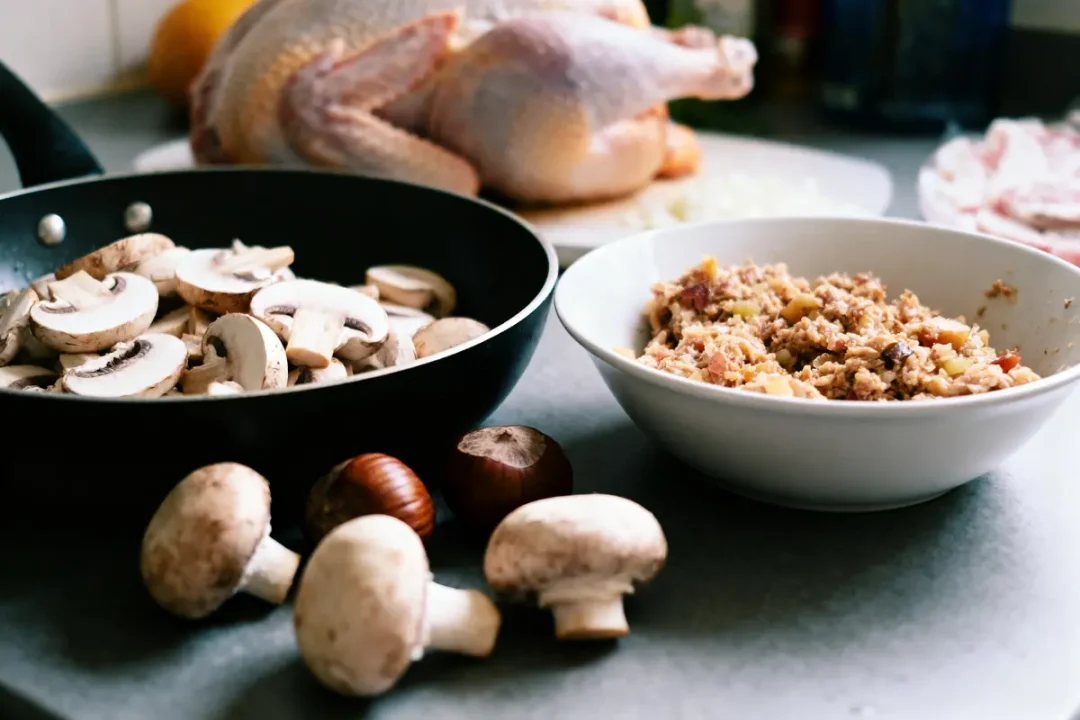 Champignons, farce dans un bol, dinde crue en arrière-plan sur un plan de travail de cuisine.