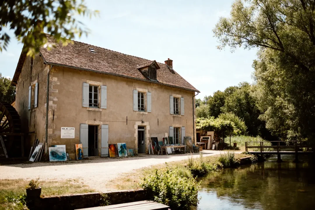 Bâtiment historique du Moulin de Launoy avec œuvres d'art exposées près d'un ruisseau paisible