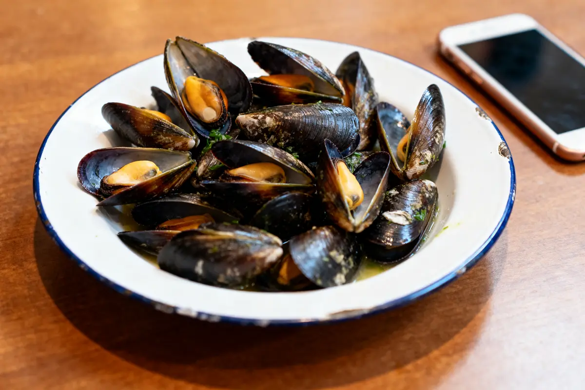 Assiette de moules cuisinées sur table bois, question combien de moules par personne.