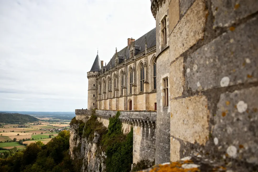 Vue latérale du Château de Bouthéon perché sur une falaise dominant la vallée verdoyante