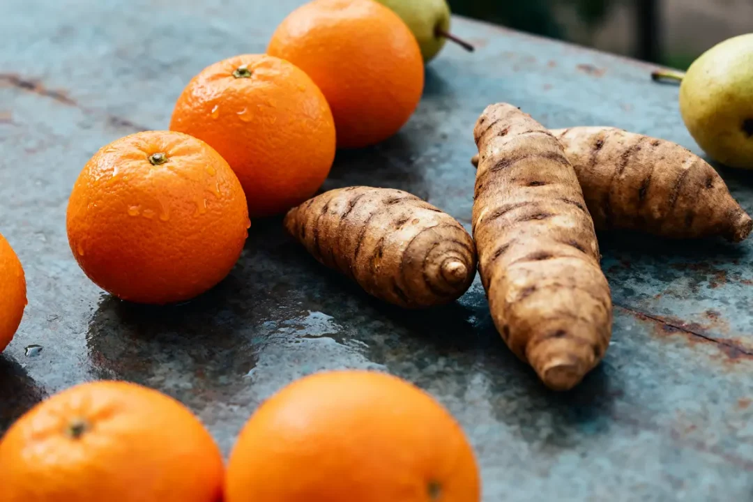 Oranges et topinambours posés sur une table métallique avec un fruit en arrière-plan