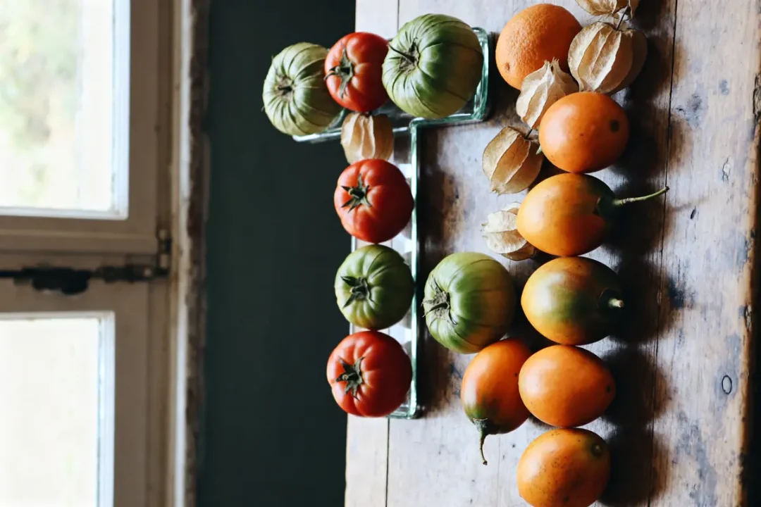 Tomates rouges et vertes disposées en forme de T avec des tamarillos oranges.
