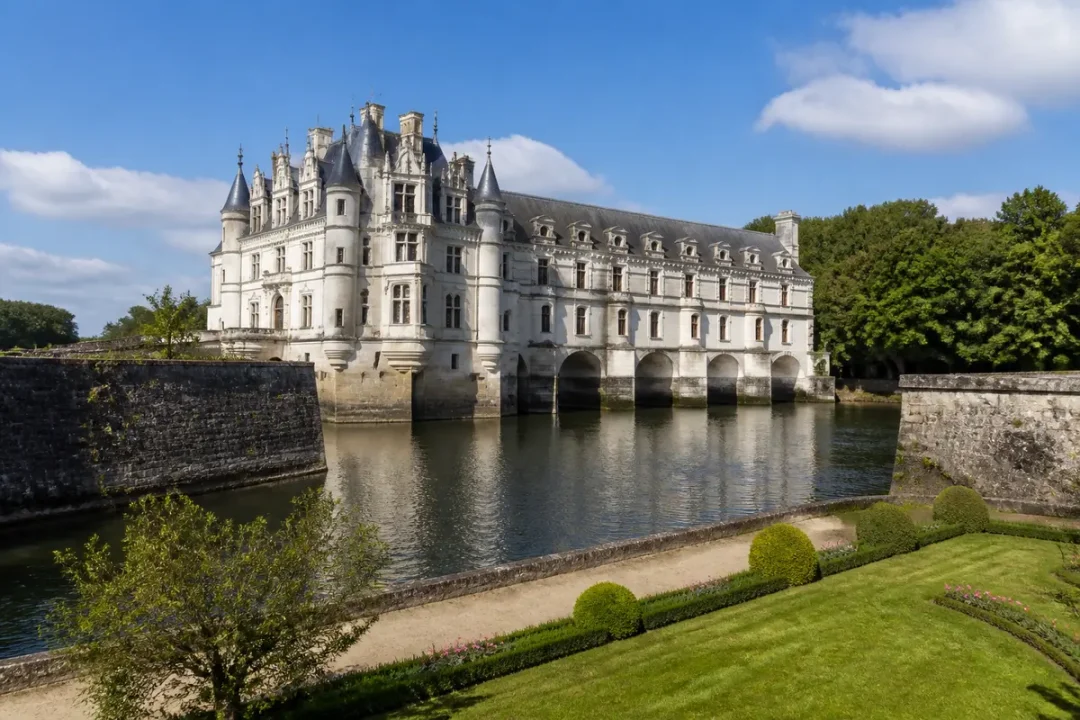 Château de la Renaissance française entouré d'eau, avec jardins et ciel bleu. Architecture élégante et historique.