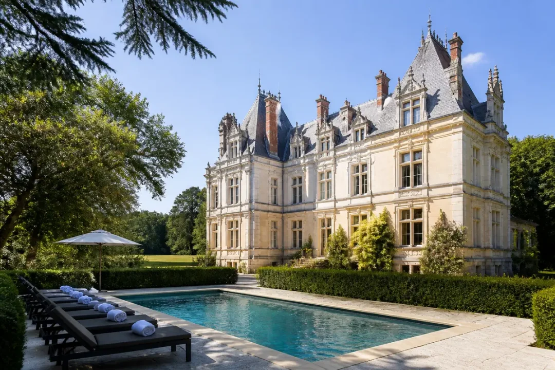 Château élégant avec piscine, transats, arbres et ciel bleu, offrant un cadre luxueux et paisible.