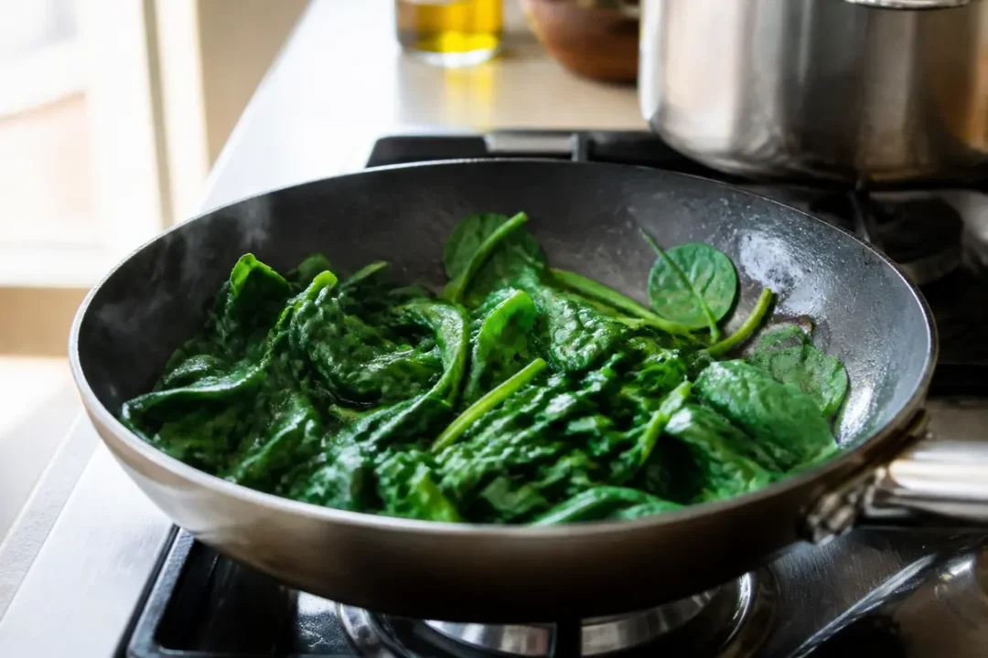 Épinards frais cuisant dans une poêle, sur cuisinière, éclairage naturel en cuisine.