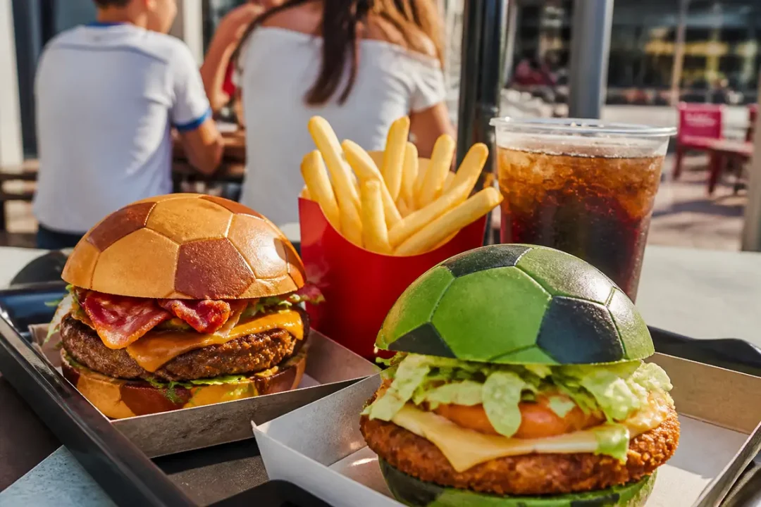 Assiettes avec hamburgers au pain en forme de ballon de football, frites et boisson gazeuse.