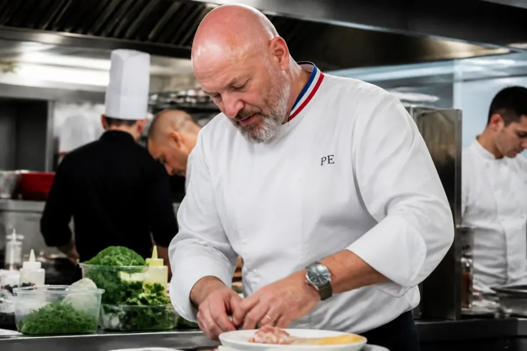 Chef cuisinier préparant un plat dans une cuisine professionnelle, entouré de chefs en tenue blanche.