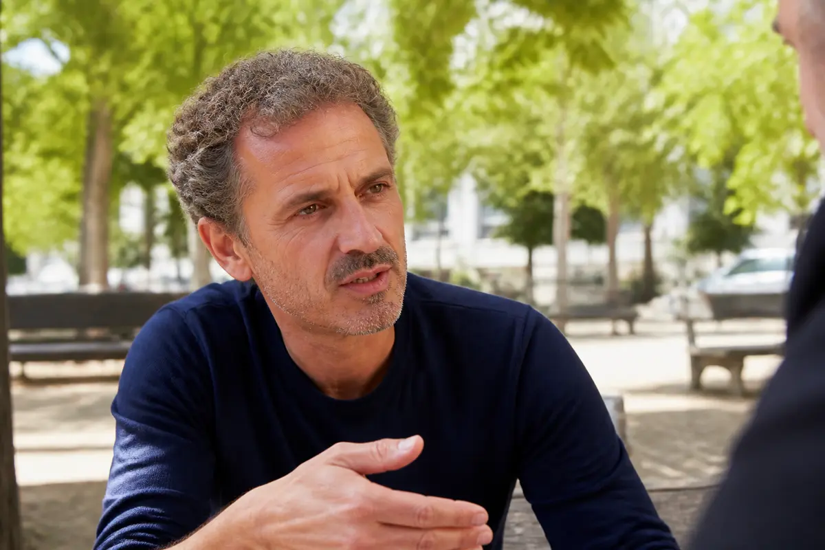 Homme discutant sérieusement à l'extérieur, parc arboré, interaction avec un interlocuteur non visible.